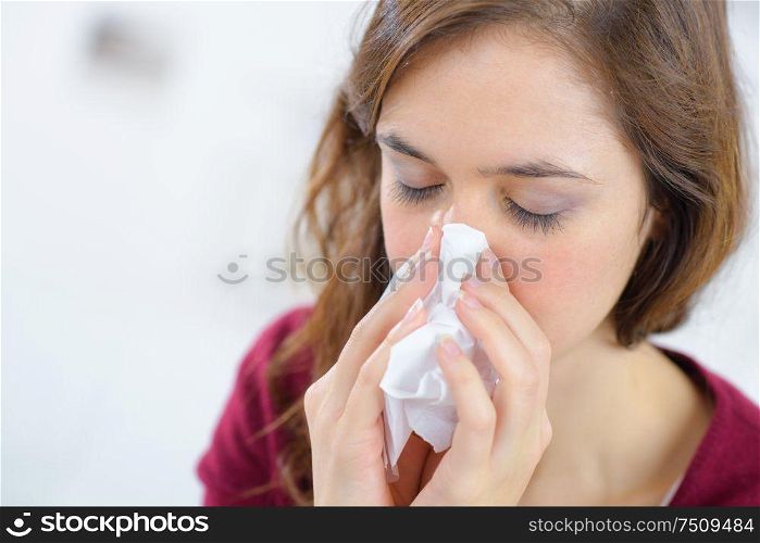 young woman blowing nose on tissue against white background