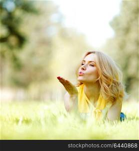 Young woman blows a kiss lying on green grass meadow