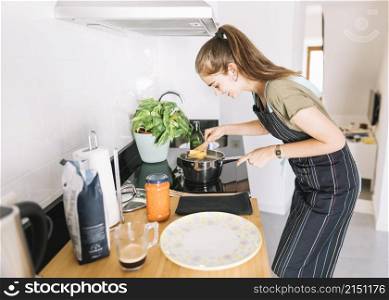 young woman boiling rigatoni pasta sauce pan electric stove