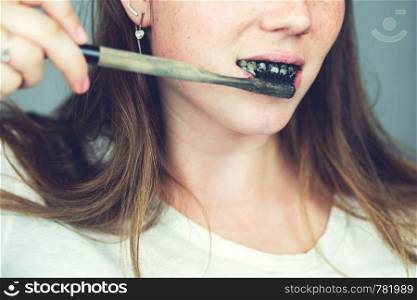 young woman brushing her teeth with a black tooth paste with active charcoal, and black tooth brush on white background for Teeth whitening clean. young woman brushing her teeth with a black tooth paste with active charcoal, and black tooth brush on white background for Teeth whitening