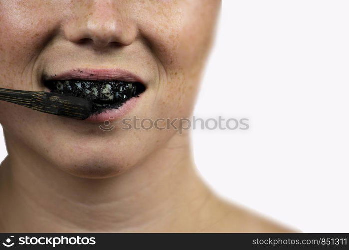 young woman brushing her teeth with a black tooth paste with active charcoal, and black tooth brush on white background for Teeth whitening clean. young woman brushing her teeth with a black tooth paste with active charcoal, and black tooth brush on white background for Teeth whitening