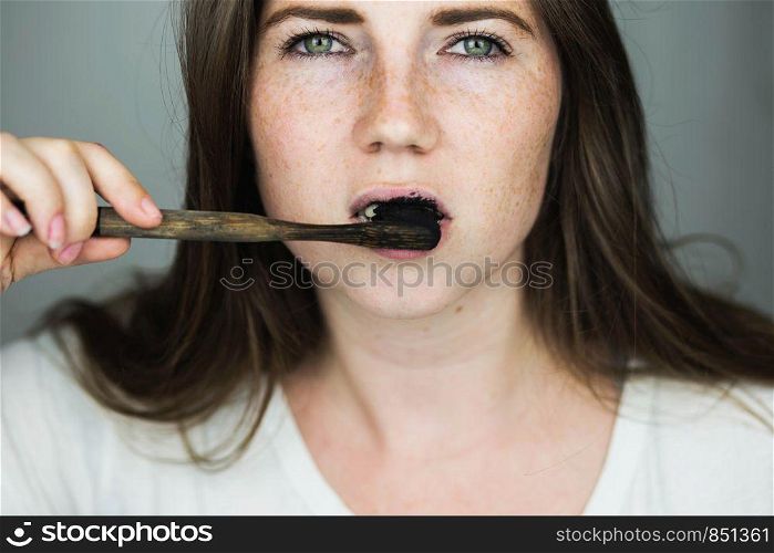 young woman brushing her teeth with a black tooth paste with active charcoal, and black tooth brush on white background for Teeth whitening clean. young woman brushing her teeth with a black tooth paste with active charcoal, and black tooth brush on white background for Teeth whitening