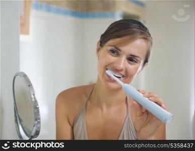 Young woman brushing teeth with electric toothbrush
