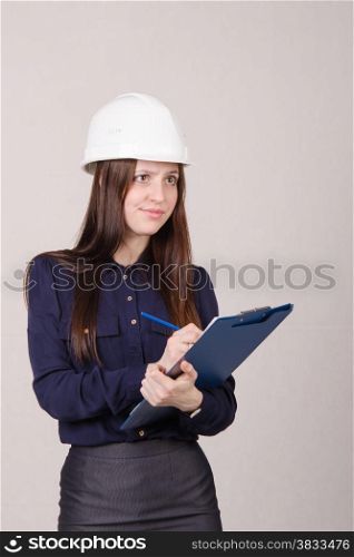 Young woman builder in helmet standing with a folder in hand