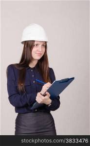 Young woman builder in helmet standing with a folder in hand