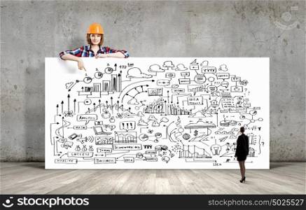 Young woman builder wearing helmet and holding banner with business plan. Development project