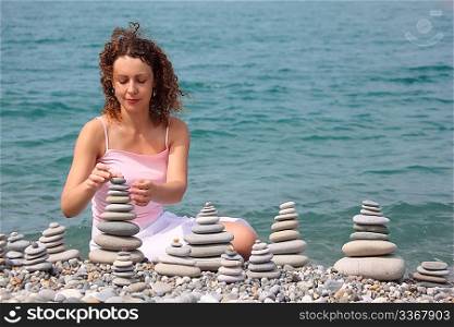 young woman builds stone stacks on pebble beach, horizontal shot
