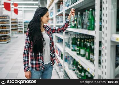 Young woman buying mineral water in supermarket. Female customer on shopping in hypermarket, department of beverages