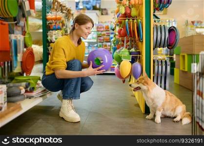 Young woman buying new toy for her corgi dog at pet shop. Happy female shopping with domestic animal on weekend. Young woman buying new toy for her corgi dog at pet shop