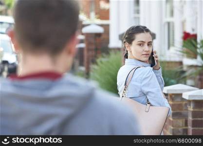 Young Woman Calling For Help On Mobile Phone Whilst Being Stalked On City Street By Man
