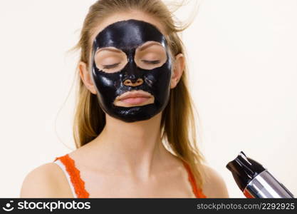 Young woman carbo black peel-off mask on her face, girl drying cosmetic to removing it, using hair dryer. Beauty treatment. Skin care.. Girl drying peel-off black mask on face