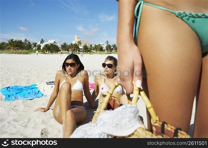 Young woman carrying beach bag, friends in background