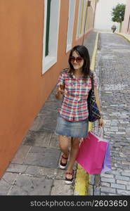 Young woman carrying shopping bags and using a mobile phone, Old San Juan, San Juan, Puerto Rico