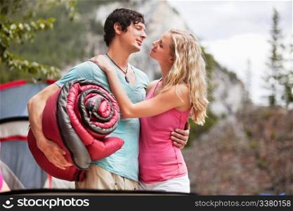 Young woman carrying sleeping bag and embracing woman while camping