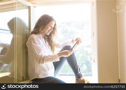 Young woman catching some sun at the balcony while using her new smartphone