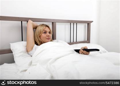 Young woman changing channels with remote control in bed