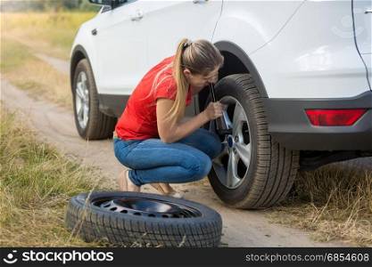 Young woman changing flat tire in field