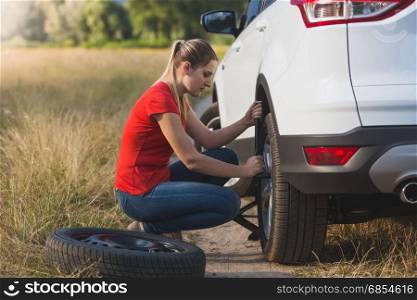 Young woman changing flat tire in field
