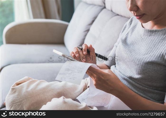 Young woman checking bills and using smart phone and calculating expenses in the living room at home