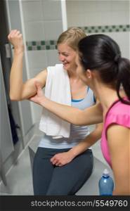 Young woman checking friend&rsquo;s muscles in changing room at gym