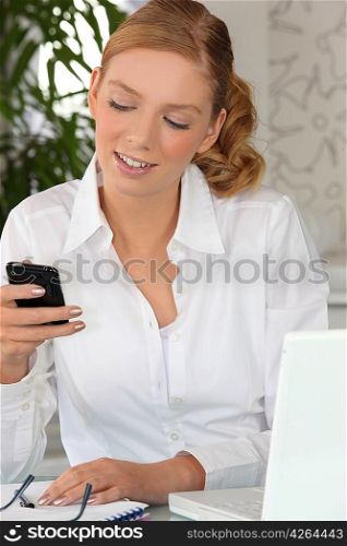 Young woman checking her cellphone at her desk