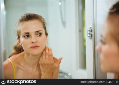 Young woman checking her face in mirror in bathroom
