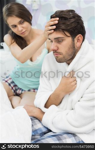 Young woman checking man&rsquo;s temperature on bed