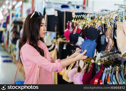 young woman choosing and buying bra in shopping store