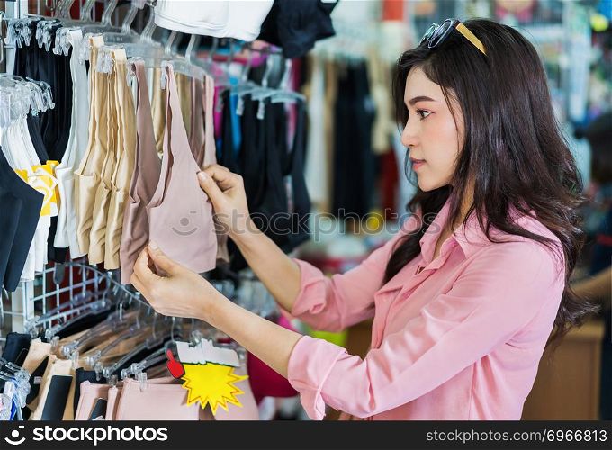 young woman choosing and buying bra in shopping store