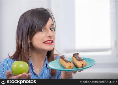 young woman choosing between an apple and a chocolate pastry