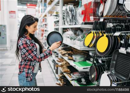 Young woman choosing frying pan in supermarket. Female customer on shopping in hypermarket, products for the kitchen