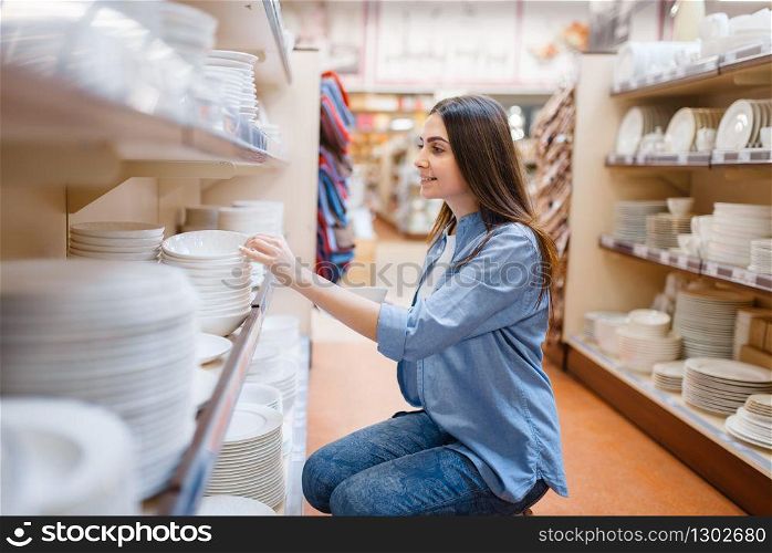 Young woman choosing plates in houseware store. Female person buying home goods in market, lady in kitchenware supply shop. Young woman choosing plates in houseware store