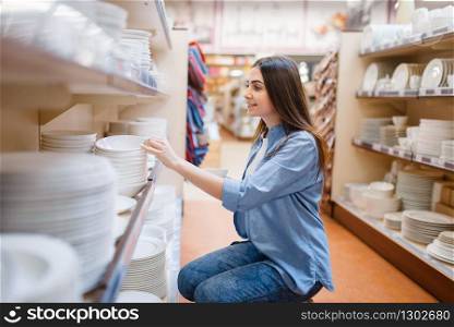 Young woman choosing plates in houseware store. Female person buying home goods in market, lady in kitchenware supply shop. Young woman choosing plates in houseware store