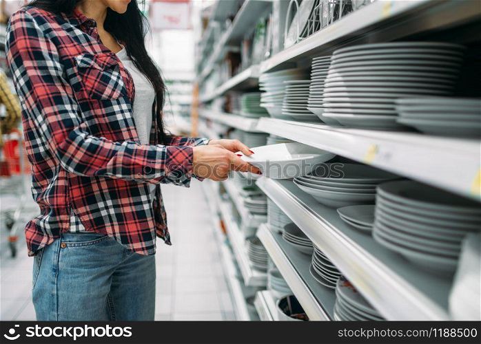 Young woman choosing plates in supermarket. Female customer on shopping in hypermarket, products for the kitchen