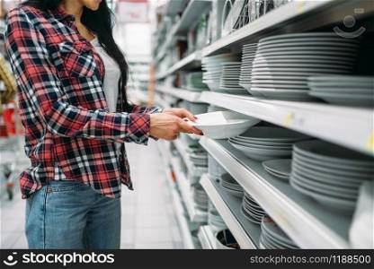 Young woman choosing plates in supermarket. Female customer on shopping in hypermarket, products for the kitchen
