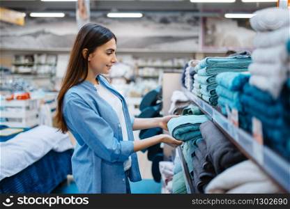 Young woman choosing towel in bed linen store. Female person buying home goods in market, lady in bedding shop. Young woman choosing towel in bed linen store