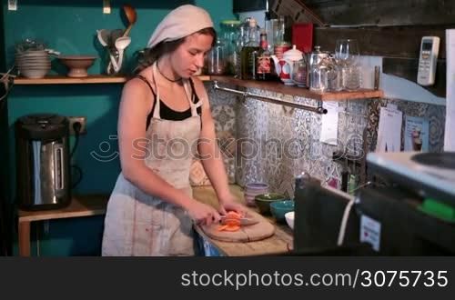 Young woman chopping organic carrot into slices on wooden cutting board in the kitchen