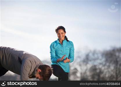 Young woman clapping man doing push up training in park