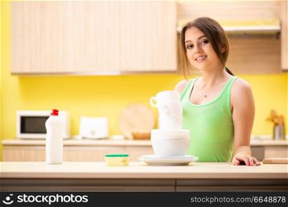 Young woman cleaning and washing dishes in kitchen