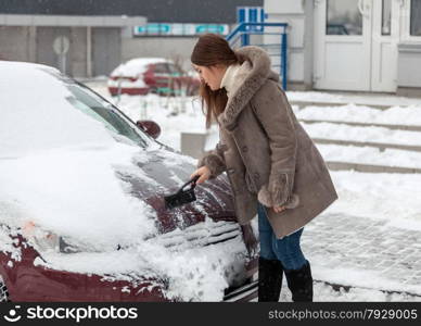 Young woman cleaning her car after snow blizzard