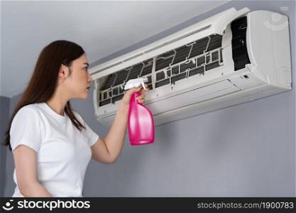 young woman cleaning the air conditioner indoors at home