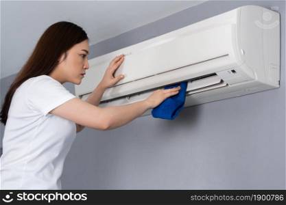 young woman cleaning the air conditioner with cloth at home