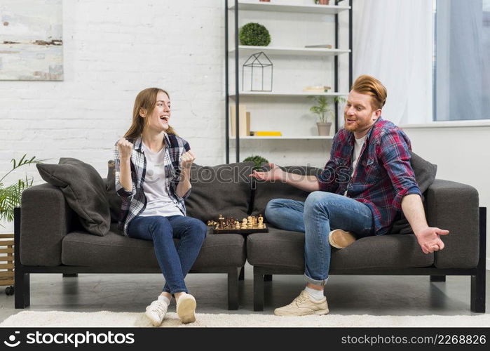 young woman clenching her fist with joy looking his boyfriend shrugging while playing chess