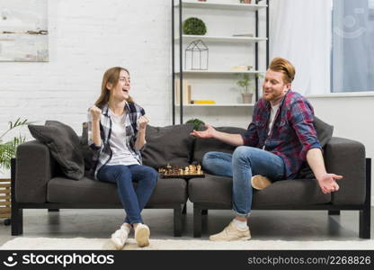 young woman clenching her fist with joy looking his boyfriend shrugging while playing chess