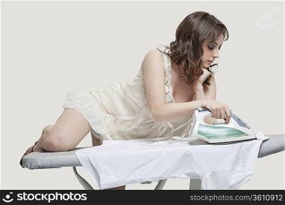 Young woman comfortably ironing shirt against gray background