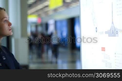 Young woman coming up to the board and looking at schematic map at the airport or shopping center