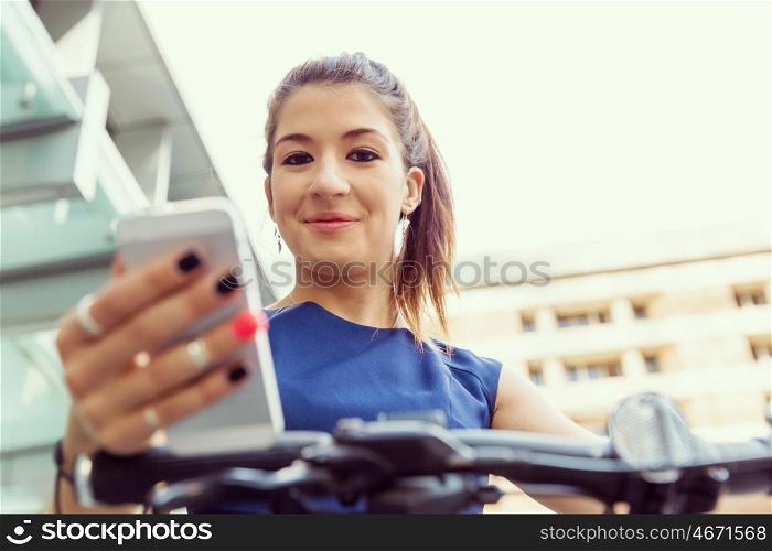 Young woman commuting on bicycle holding a mobile. Young woman in business wear on bicycle and holding mobile phone