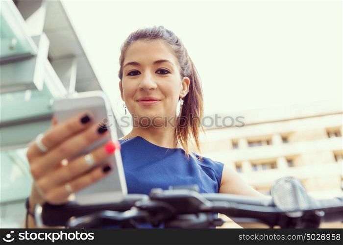 Young woman commuting on bicycle holding a mobile. Young woman in business wear on bicycle and holding mobile phone