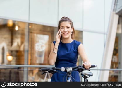 Young woman commuting on bicycle. Young woman in business wear on bicycle and holding mobile phone