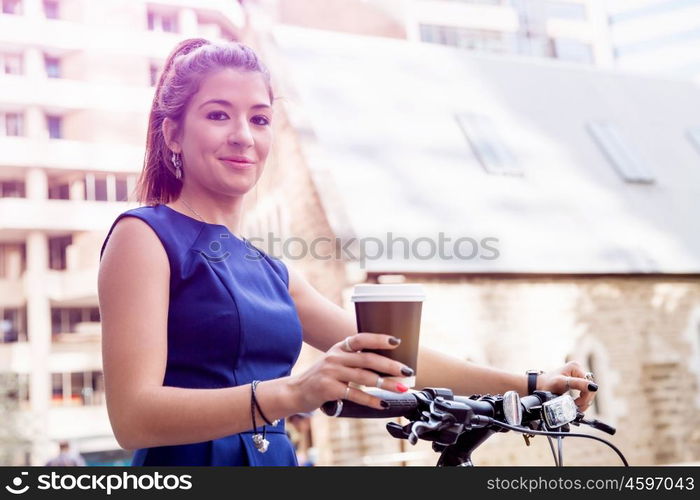 Young woman commuting on bicycle. Young woman in business wear on bicycle with a cup of coffee